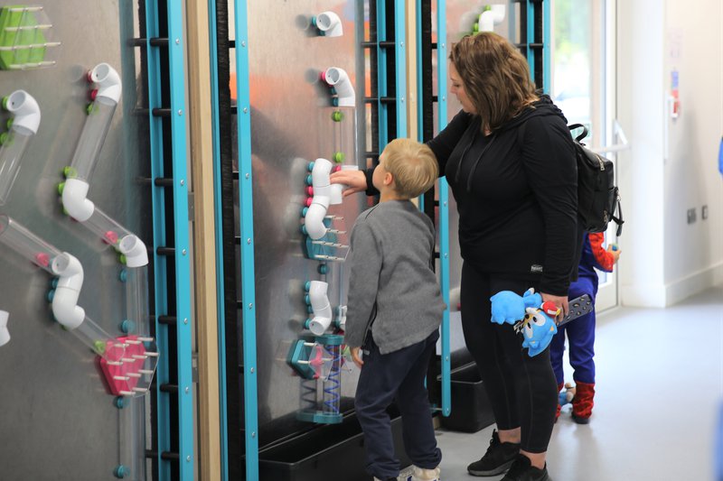 An adult and child stood interacting with a science exhibit that movable tubing.