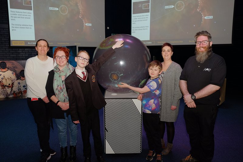 A group of six people including children stood around a science exhibit.