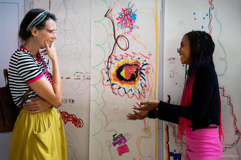 An adult and young person stood in front of some art talking and smiling.