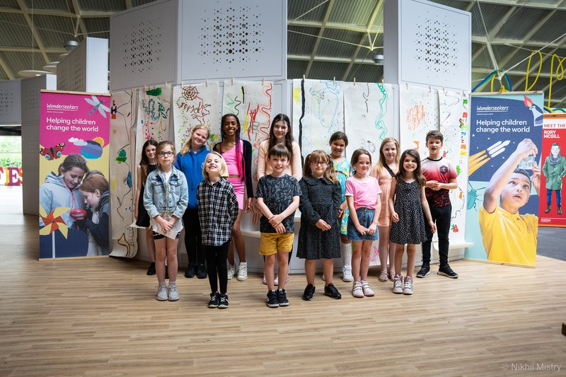 Group of children mixed genders, ages and ethnicity in front of their artwork