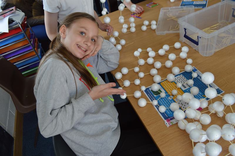 A young girl smiling at the camera showing her work