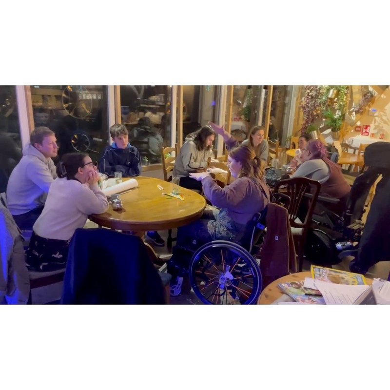 Young people and adults sat around tables talking of mixed abilities.