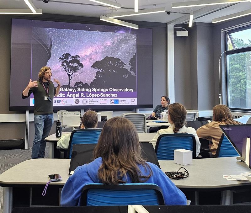 Group of kids in a classroom with a man presenting at the front of the room