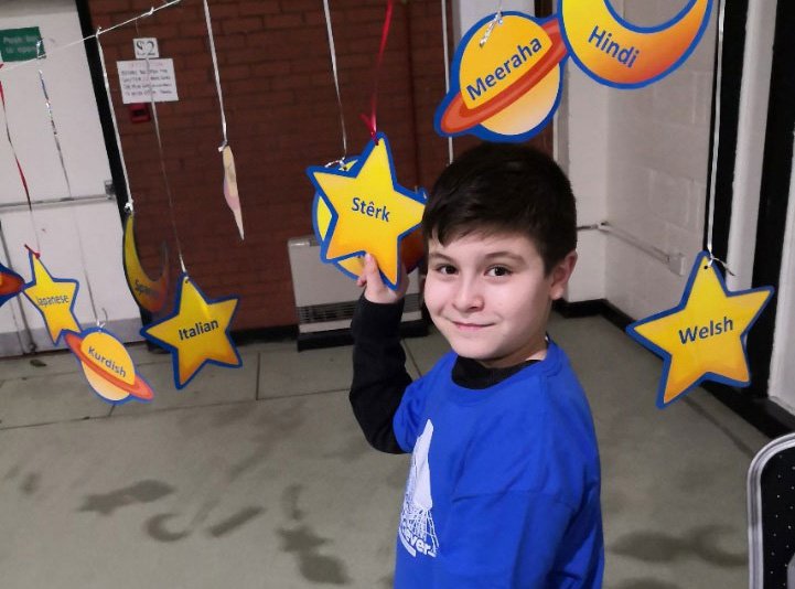 A child holding a card star, with foreign language written on it.