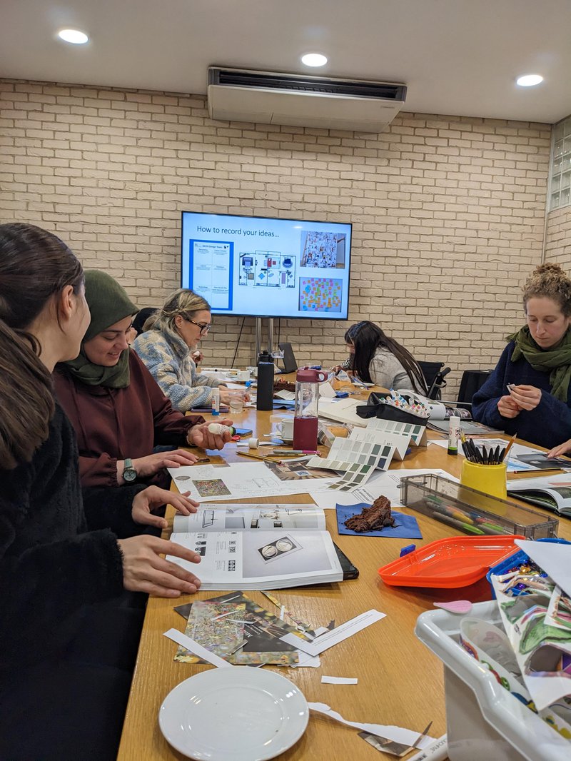 Class room with five people sat around one table working with creative items.