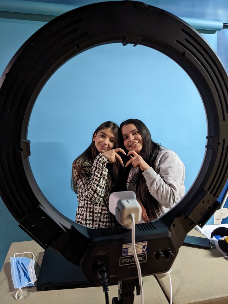 Two young people being photographed with their hands forming a heart shape together.